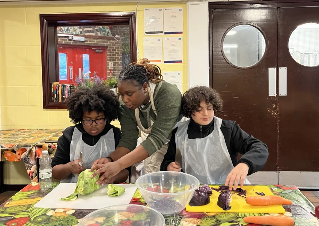 Eat club cooking and food education session at camden youth club Siding's, two boys cooking with session leader Toni